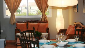 Un coin repas avec une table dressée pour quatre personnes, un canapé avec des coussins orange et un grand lampadaire.