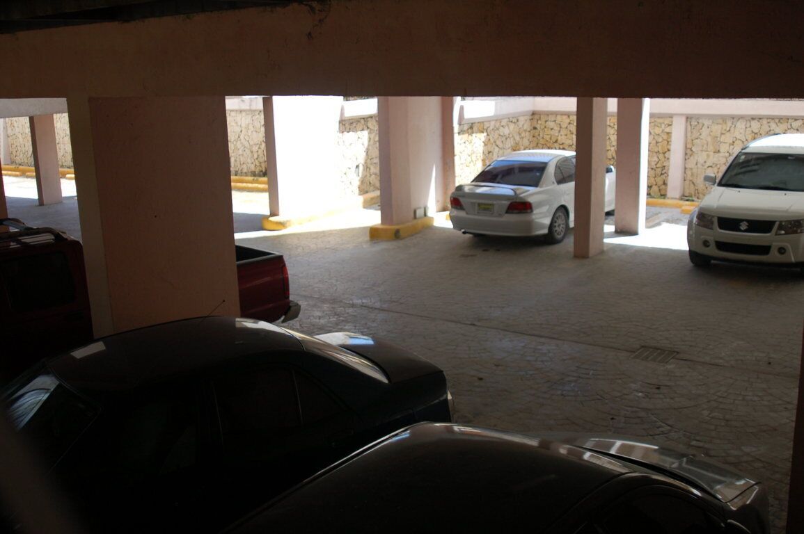 Un parking souterrain où plusieurs voitures sont garées sous une structure soutenue par des piliers.