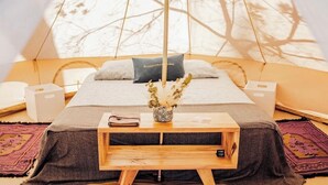 Una habitación acogedora con cama, una mesita de noche con un libro y un florero, y vistas a árboles a través de una ventana.