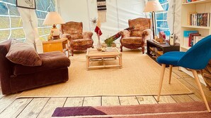 Una habitación con carpa, un sofá, sillones, una mesita de centro, una estantería y una lámpara.