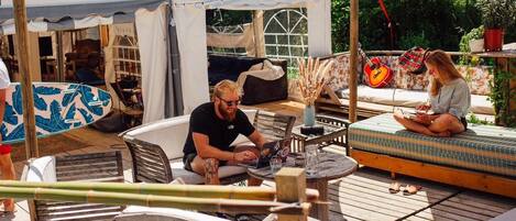 A wooden deck with outdoor seating, a covered area with a table, and a surfboard.