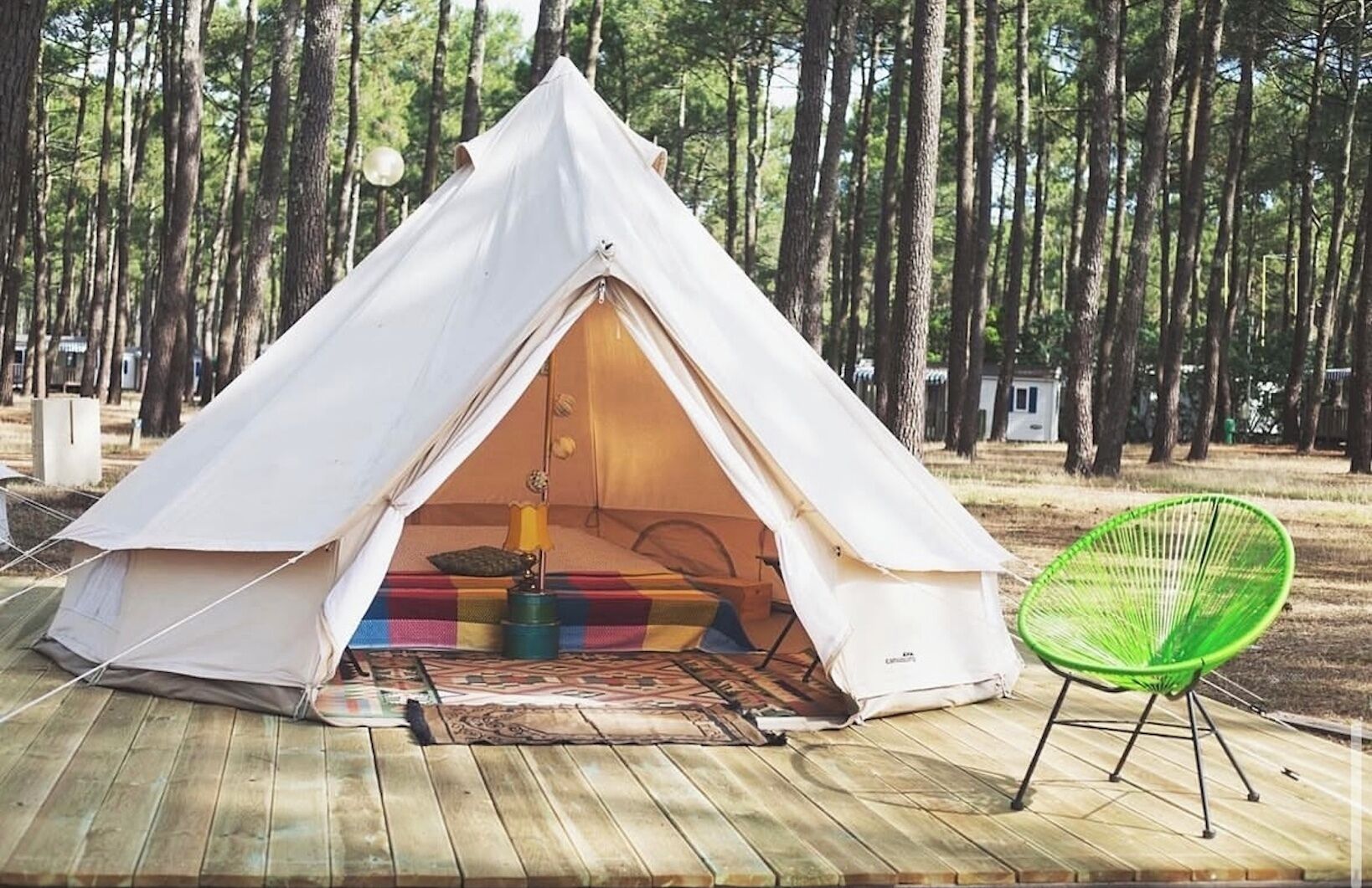 A white tent with a colorful interior, a green chair, and a wooden deck.