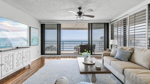 A spacious living room with a large window, a ceiling fan, and a view of the ocean. - ☀️Ebb Tide 301-Oceanfront with Fabulous Views-Pool+Hot Tub☀️ (New Smyrna Beach)