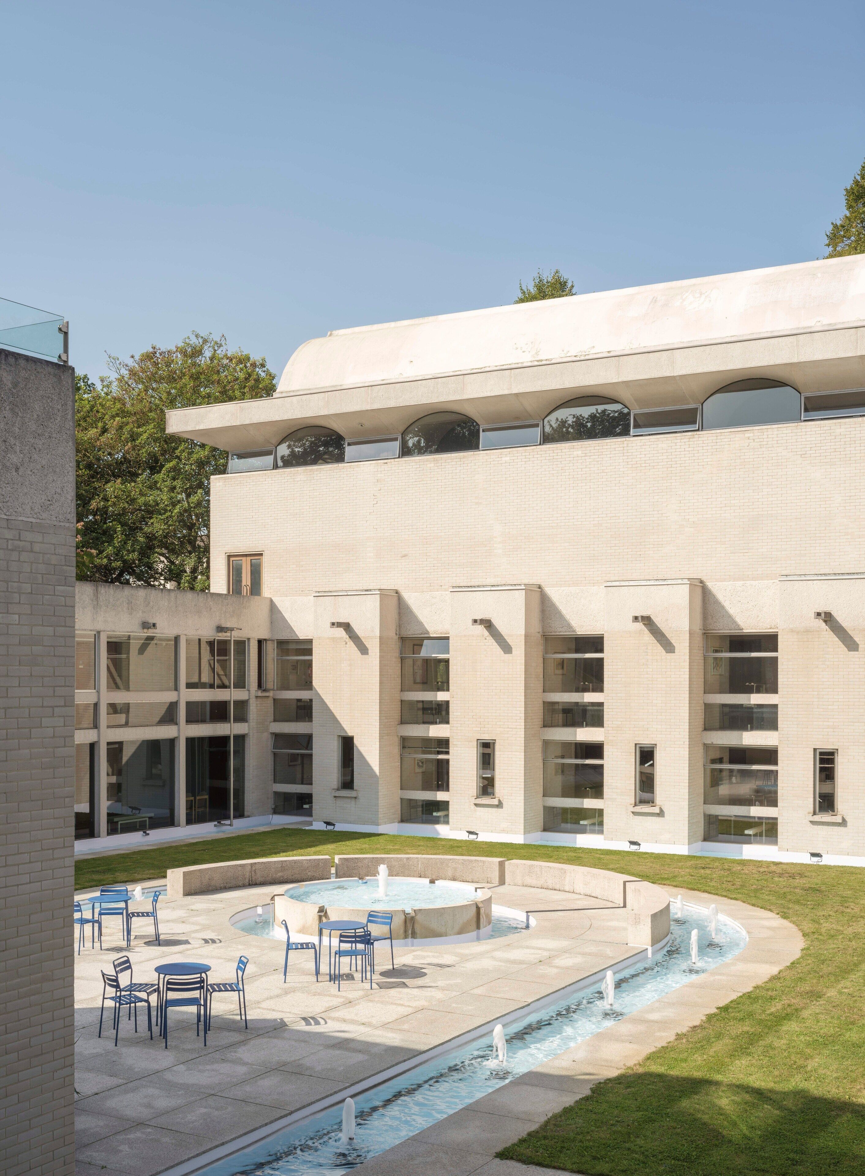 A modern building with a courtyard featuring a pool, seating area, and a fountain.