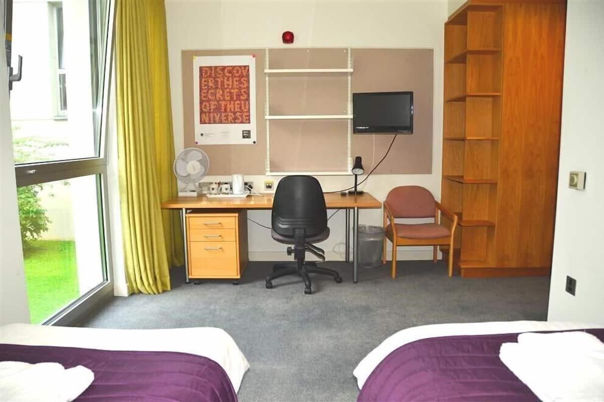 A room with two beds, a desk with a computer, a chair, a TV, and a bookshelf.