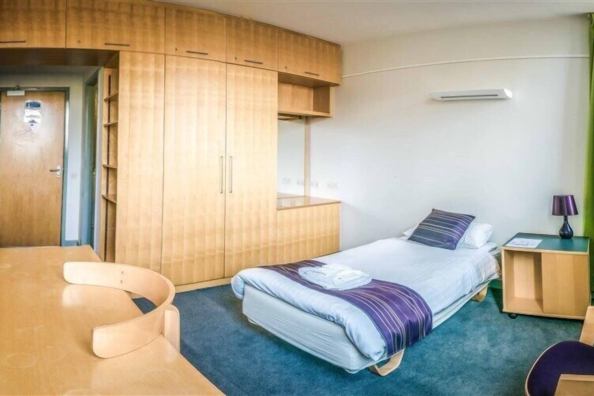 A compact hotel room with a bed, a desk, a chair, a wardrobe, and a small table.