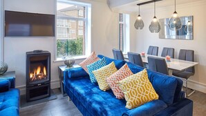 Un salon moderne avec un canapé bleu, une cheminée, un coin repas et une grande fenêtre.