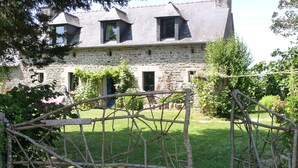 Une ferme en pierre au design traditionnel, avec une façade en pierre, de nombreuses fenêtres et un jardin bien entretenu.