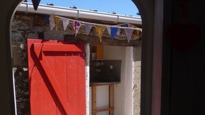 Une porte rouge qui donne sur une pièce avec un mur en pierre et une petite étagère en bois.