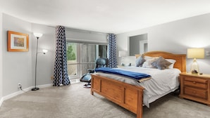 A bedroom with a wooden bed, a nightstand, a lamp, a chair, and a large window with curtains.