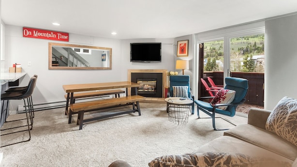 A living room with a fireplace, a TV mounted on the wall, a bench, and a sofa.