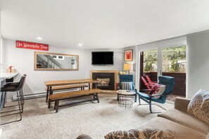 A living room with a fireplace, a TV mounted on the wall, a bench, and a sofa.
