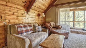 A cozy cabin interior with a wooden ceiling, a sofa set, a coffee table, and a large window providing a view of the outdoors. - Winter Hawk House (Groveland)