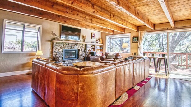 A cozy living room with a stone fireplace, leather seating, and large windows offering a view of the outdoors. - Winter Hawk House (Groveland)