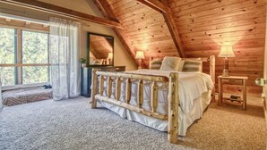 A cozy bedroom with a wooden ceiling, a bed with white bedding, a nightstand, and a lamp. - Winter Hawk House (Groveland)