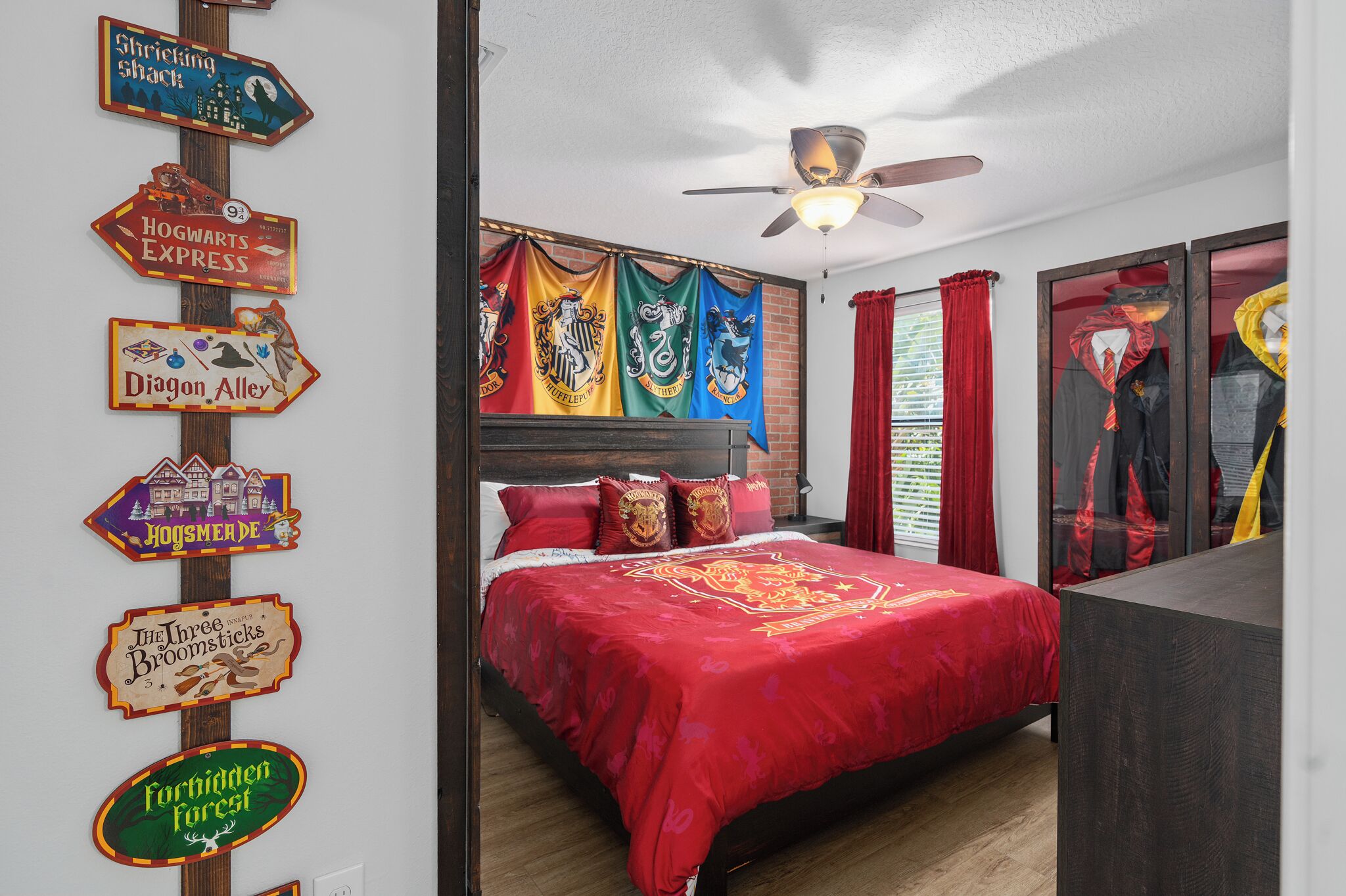 Un dormitorio con colcha roja, cabecera de madera y múltiples decoraciones con temática de Harry Potter, incluyendo pancartas y un cartel.