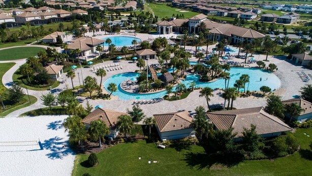 Luchtbeeld van een resort met meerdere zwembaden, palmbomen en een golfbaan op de achtergrond.