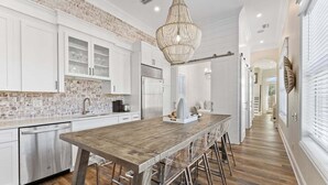 Une cuisine dotée d’un îlot central en bois, de meubles blancs et d’un mur d’accent en briques.