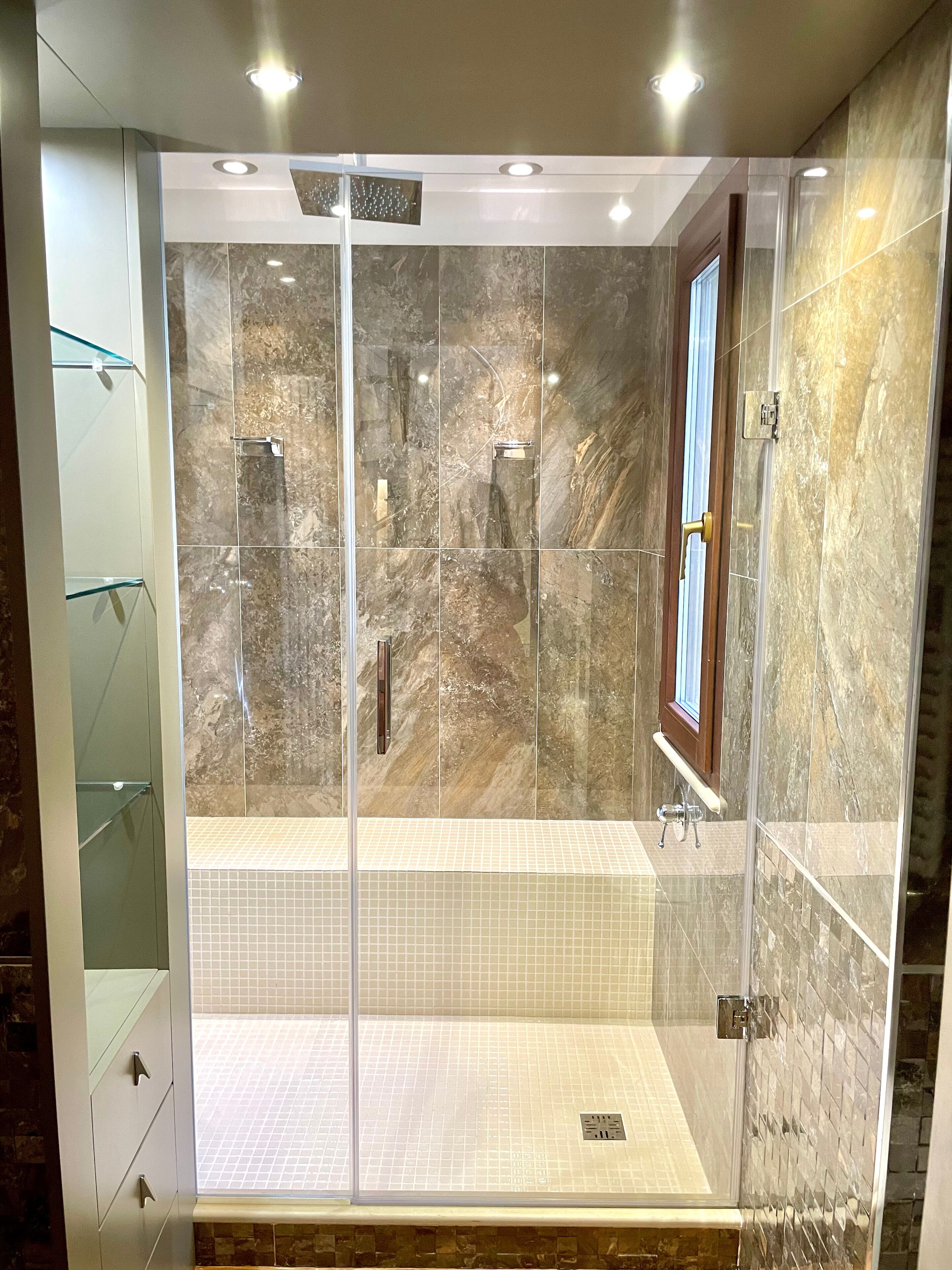 A walk-in shower with glass doors, marble walls, and a tiled floor.