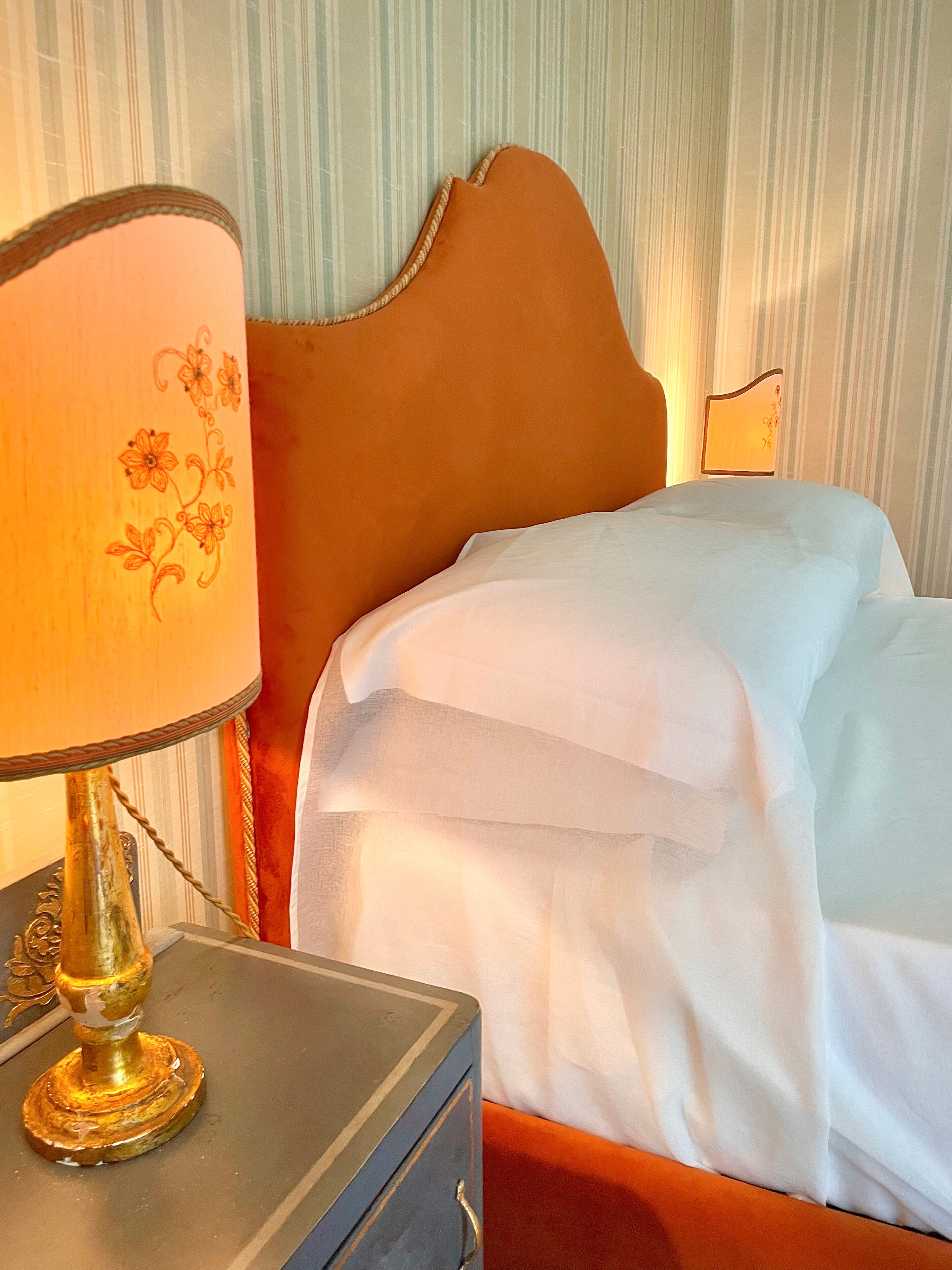 A neatly made bed with white linens, a wooden headboard, and a bedside table with a lamp.