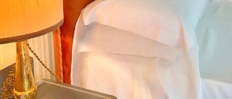 A neatly made bed with white linens, a wooden headboard, and a bedside table with a lamp.