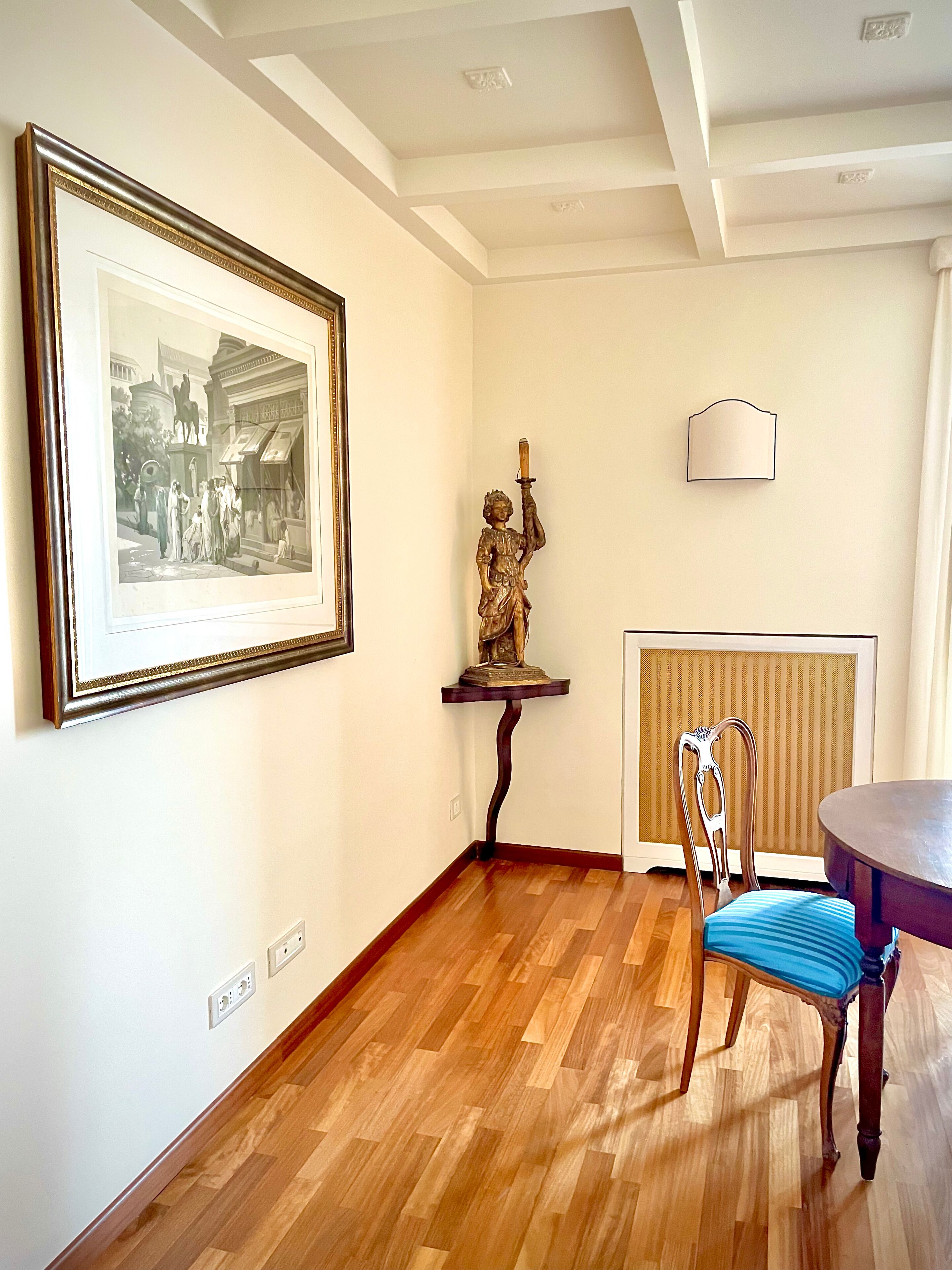 Quarto com fotografia a preto e branco emoldurada, uma estátua, um radiador e uma mesa de jantar com uma cadeira.