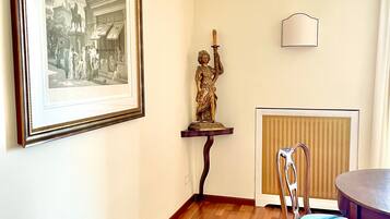 Quarto com fotografia a preto e branco emoldurada, uma estátua, um radiador e uma mesa de jantar com uma cadeira.