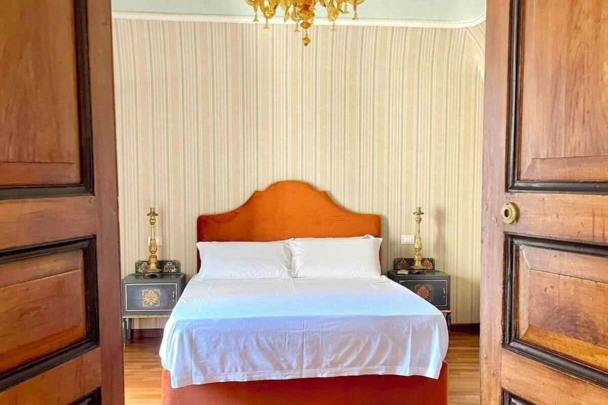 A bedroom with a wooden bed, white bedding, a chandelier, and a striped curtain.