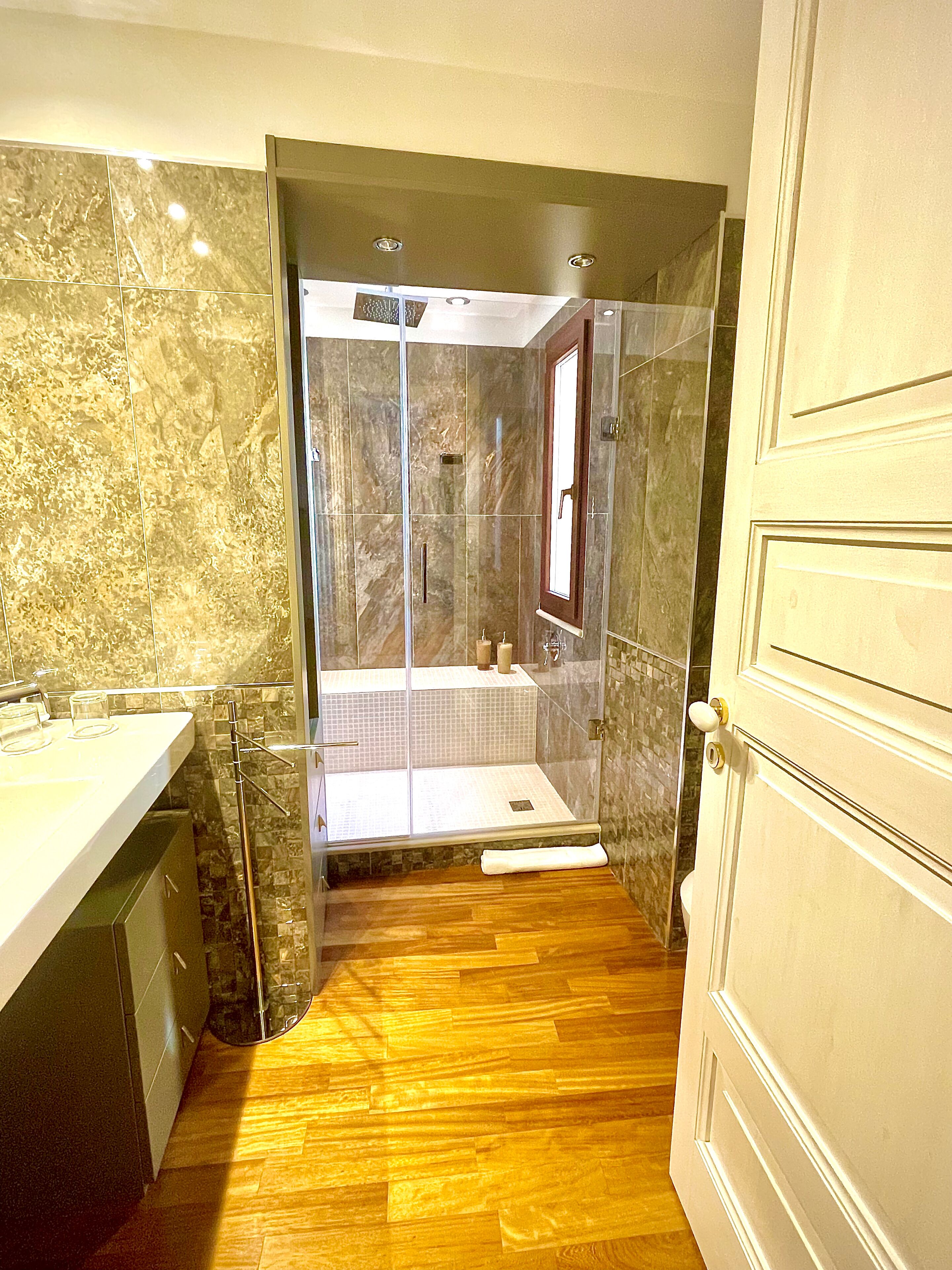 Un baño con ducha de vidrio, suelo de madera y pared de mármol.