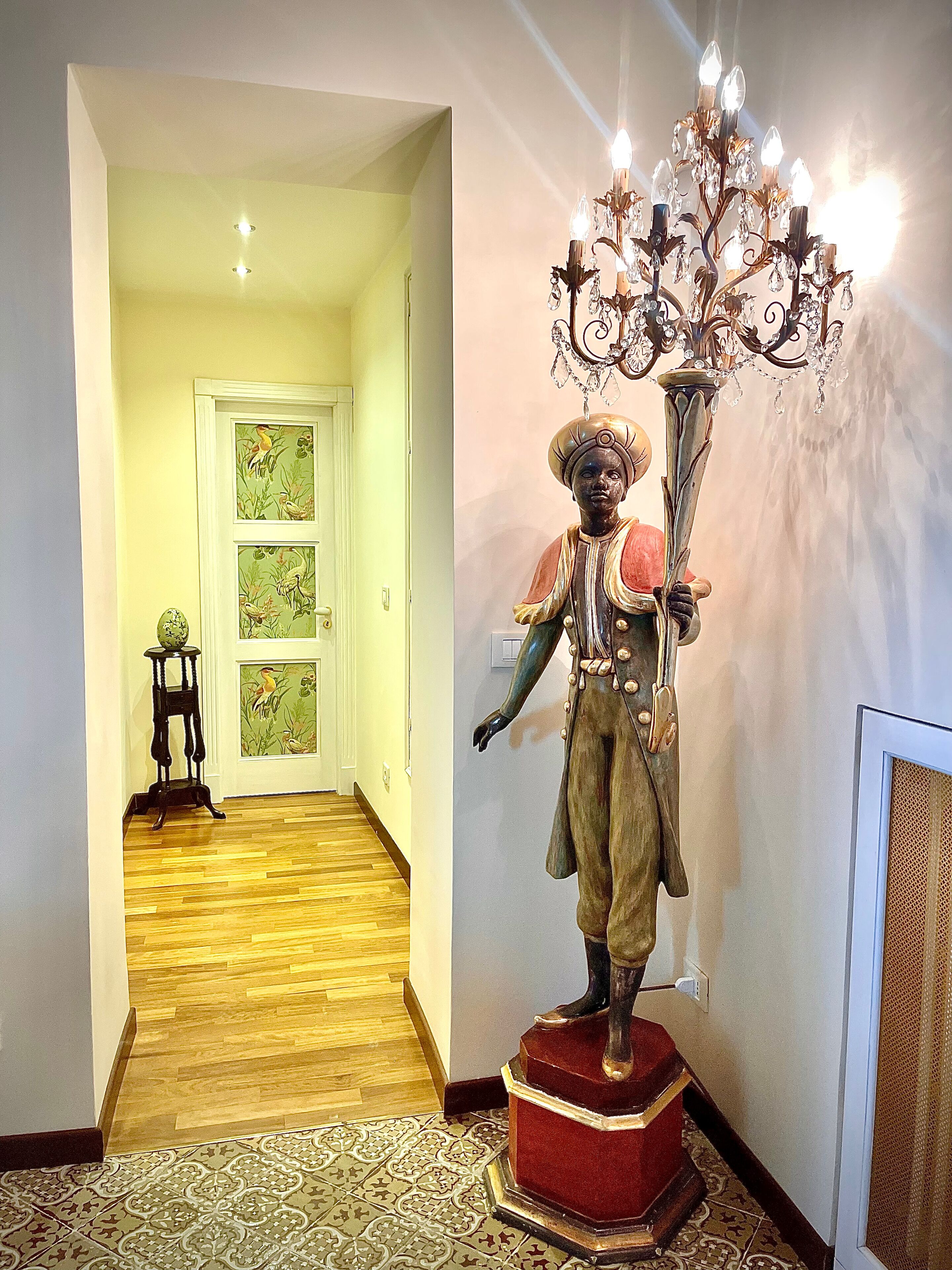 A hallway with a wooden floor, a statue on a pedestal, and a chandelier.