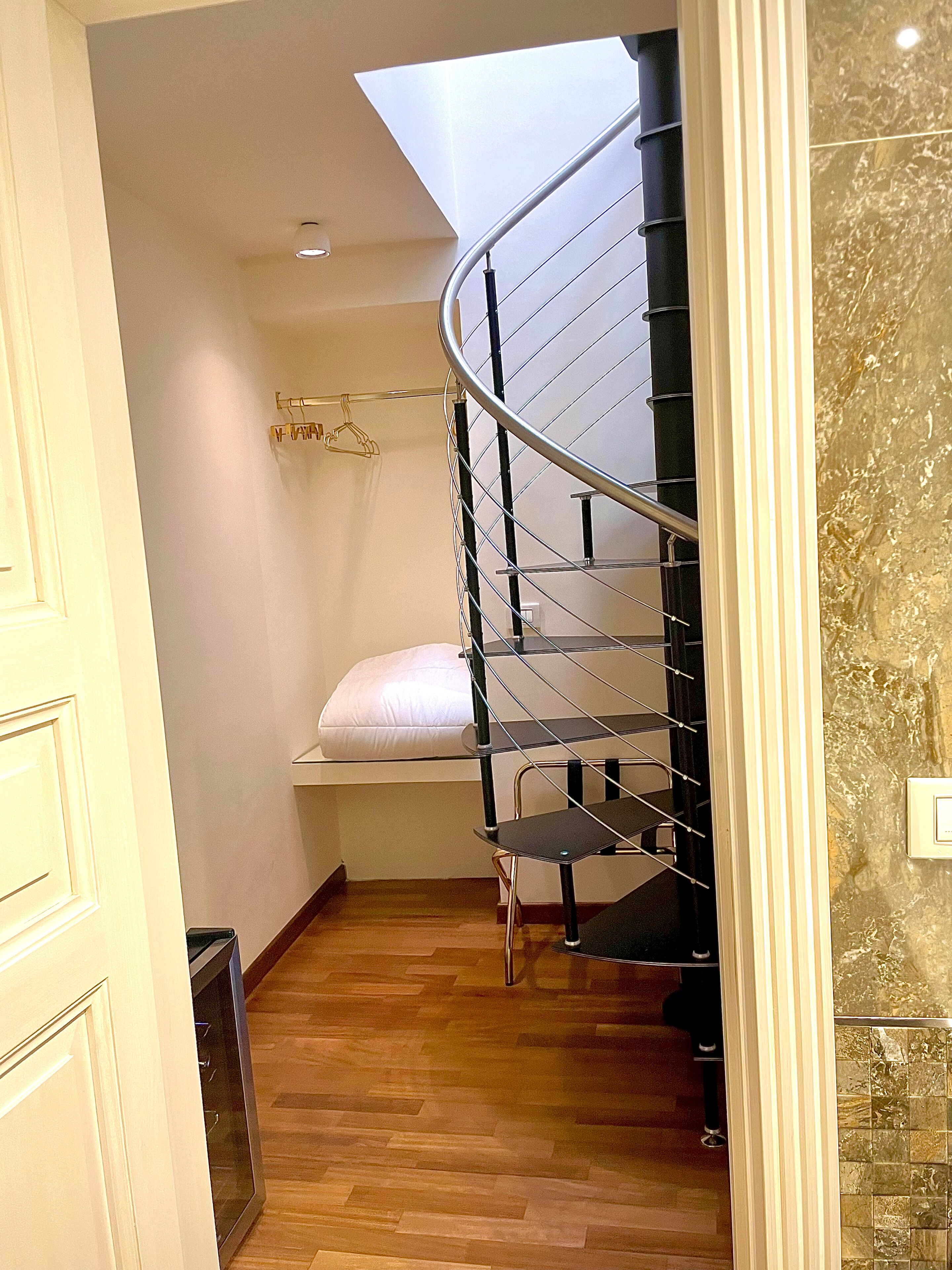A compact, modern room with a spiral staircase, a small seating area with a white cushion, and a wooden floor.
