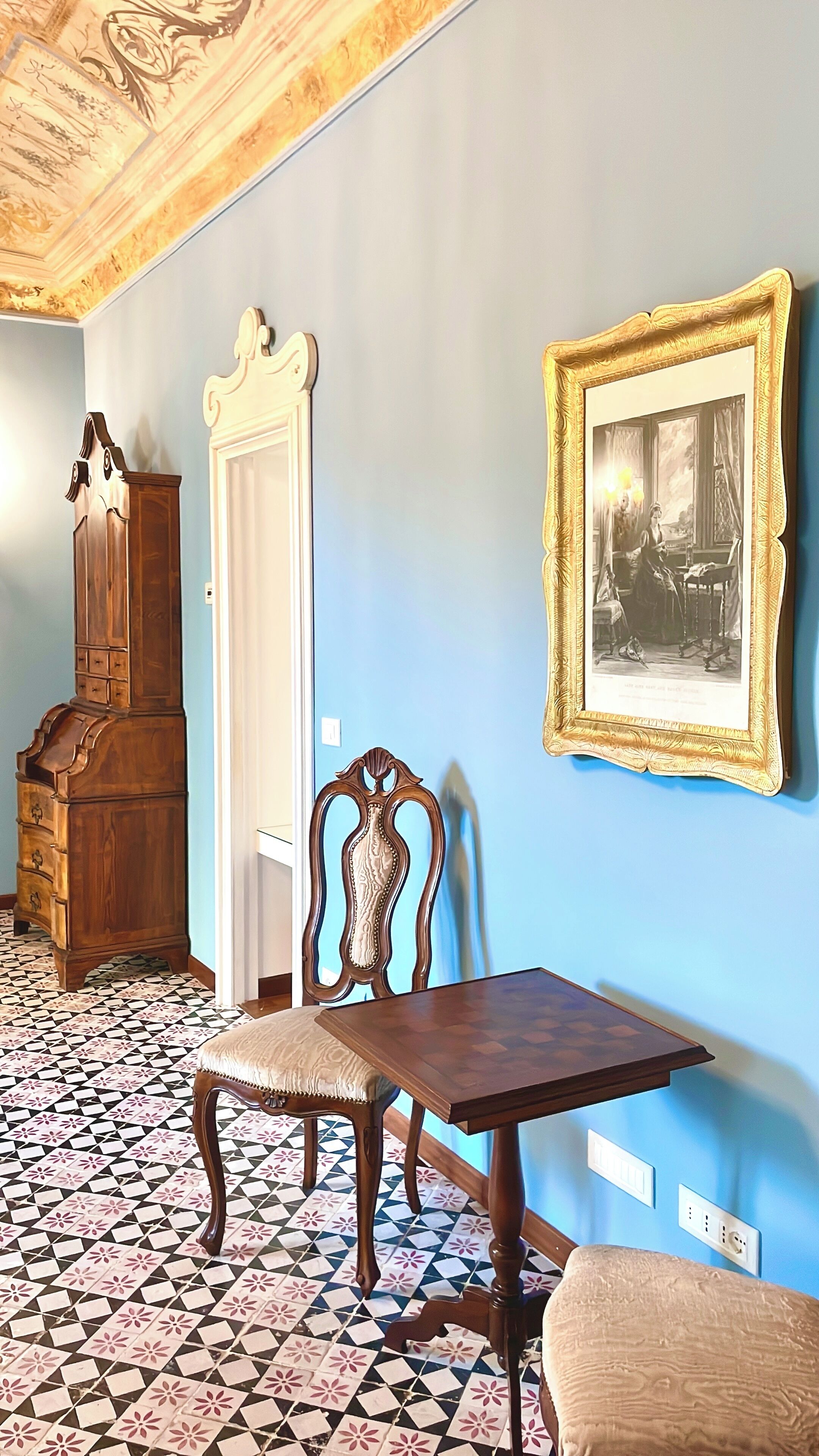 A room with a wooden cabinet, a chair, a table, and a framed picture on the wall.
