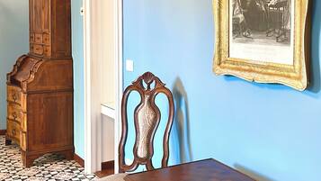 A room with a wooden cabinet, a chair, a table, and a framed picture on the wall.