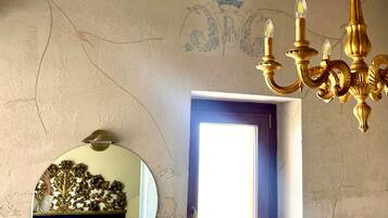 Un baño con un espejo redondo, una araña de cristal, una ventana con toallas y un estante con artículos de aseo.