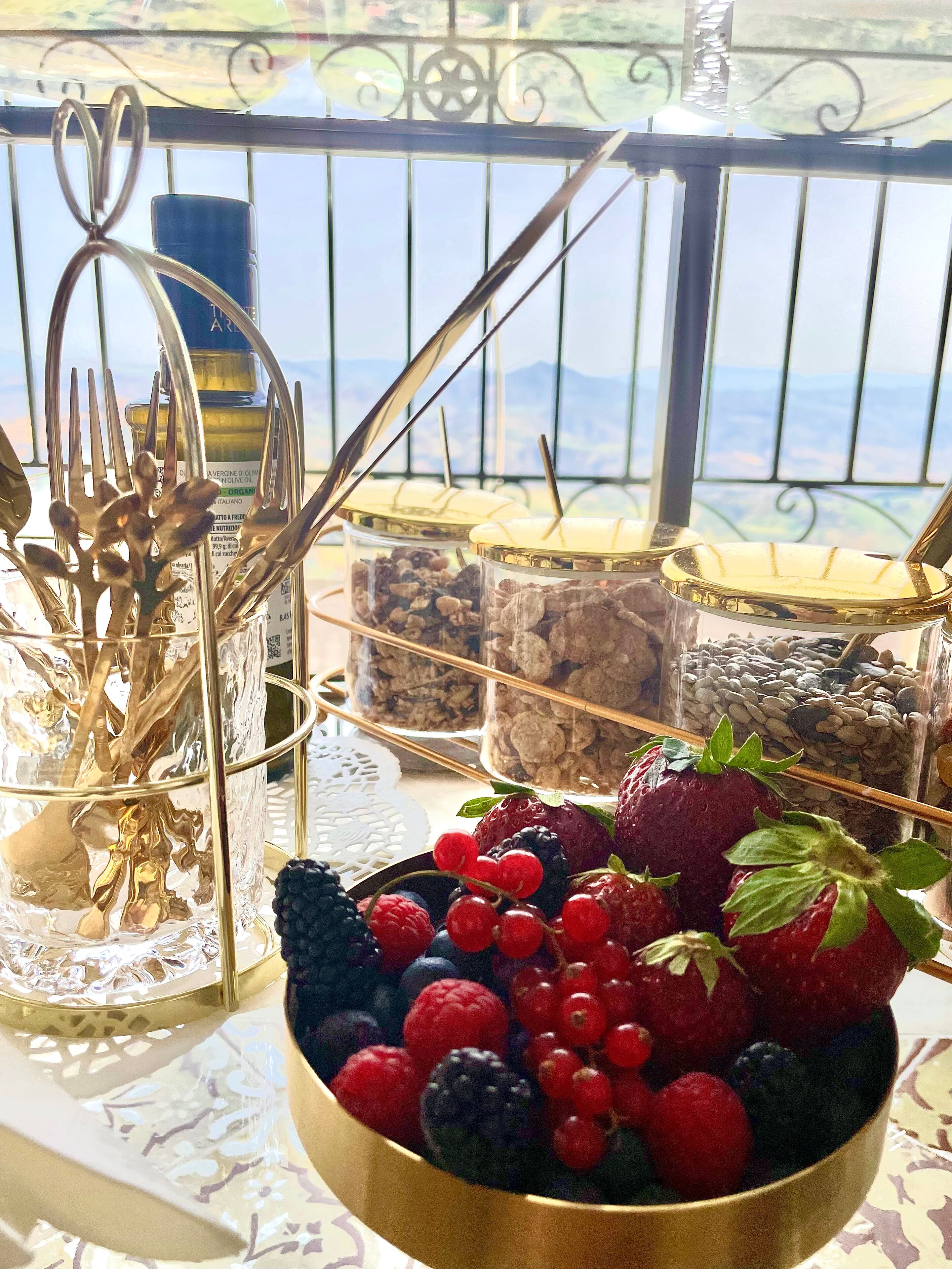 A table with a bowl of fresh berries, a glass jar with nuts, and a metal utensil holder.