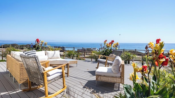 A wooden deck with wicker furniture, a table, and chairs, overlooking the ocean. - Windows on the Waves (Santa Cruz)