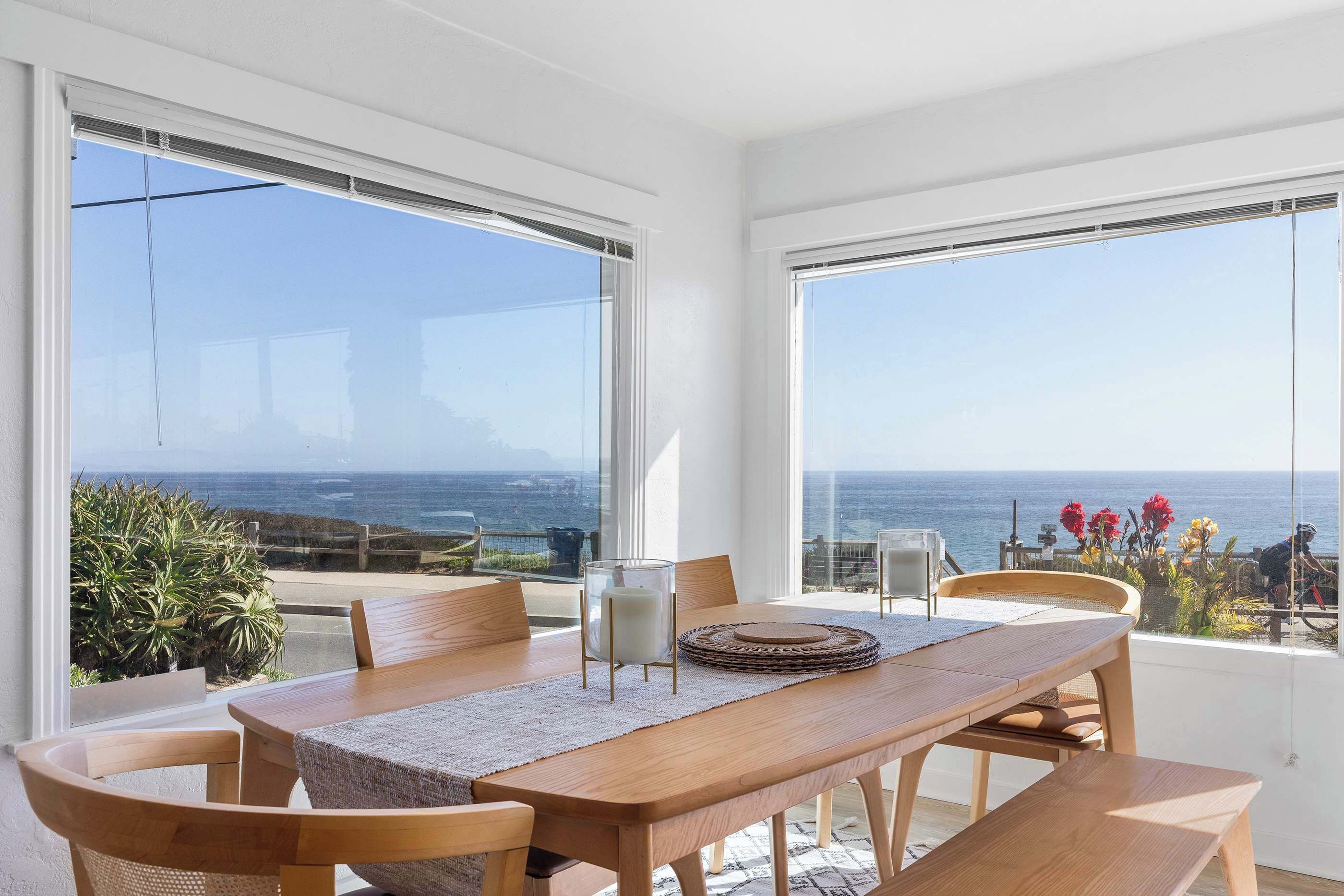 Un comedor con mesa de madera, sillas y vista al océano.