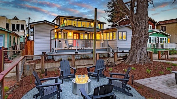 Ein zweistöckiges Haus mit Terrasse, umgeben von einem Holzzaun und mit Gartenmöbeln inklusive Feuerstelle.