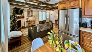 A modern living room with a sofa, a dining table with a vase of flowers, and a kitchen area with wooden cabinets and a stainless steel refrigerator. - Happy Valley Spacious Family Townhome.Dog Friendly.Minutes to Blue Mountain (Collingwood)