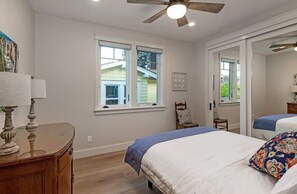 A bedroom with two beds, a ceiling fan, a window with a view, and a wooden dresser.