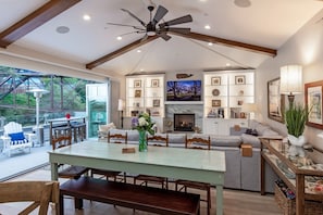 A spacious living area with a fireplace, a ceiling fan, and a dining area with a table and chairs. - Rivervfront Upper Duplex w/ & Firepit on the Patio (Capitola)