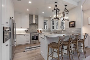 A modern kitchen with white cabinetry, stainless steel appliances, and a central island with bar stools. - Rivervfront Upper Duplex w/ & Firepit on the Patio (Capitola)