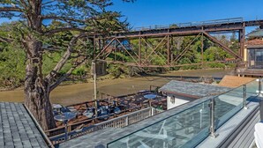 Vista al río con un puente, asientos al aire libre y barandilla de cristal con vistas al agua.