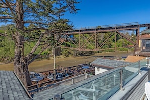 A riverside view with a bridge, outdoor seating, and a glass railing overlooking the water. - Rivervfront Upper Duplex w/ & Firepit on the Patio (Capitola)