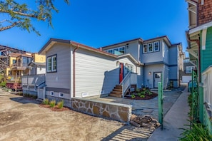 A row of modern houses with a stone retaining wall in front, a clear blue sky, and a well-maintained lawn. - Rivervfront Upper Duplex w/ & Firepit on the Patio (Capitola)