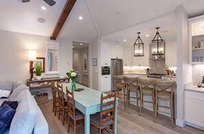 A modern kitchen with white cabinetry, a dining area with a blue table and wooden chairs, and pendant lighting.