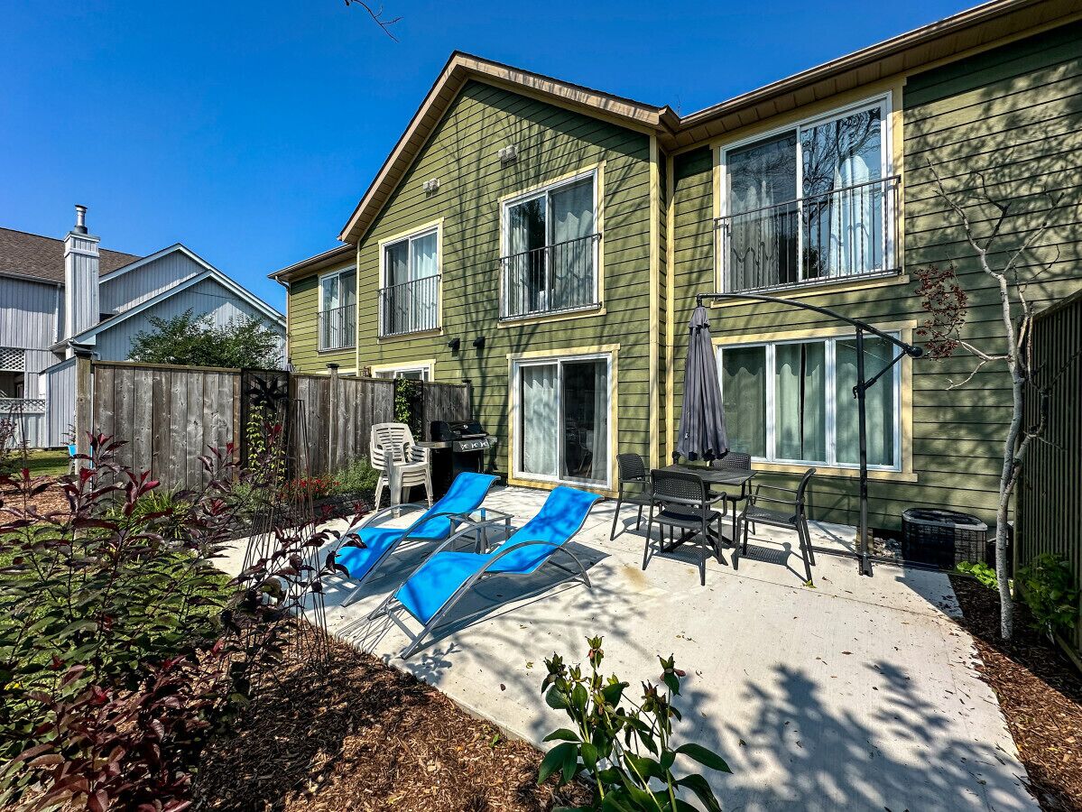 Une maison à deux étages avec un patio à l’arrière, une piscine et un espace extérieur aménagé avec des sièges.