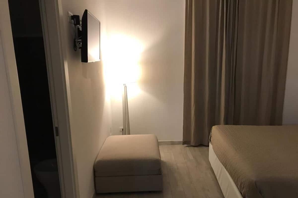 Une chambre d’hôtel avec un lit, une table de chevet, une lampe et une fenêtre avec des rideaux.