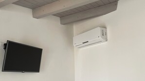 A room with a flat-screen TV mounted on the wall, a ceiling fan, and a white air conditioning unit. - La Coffa (Noto)