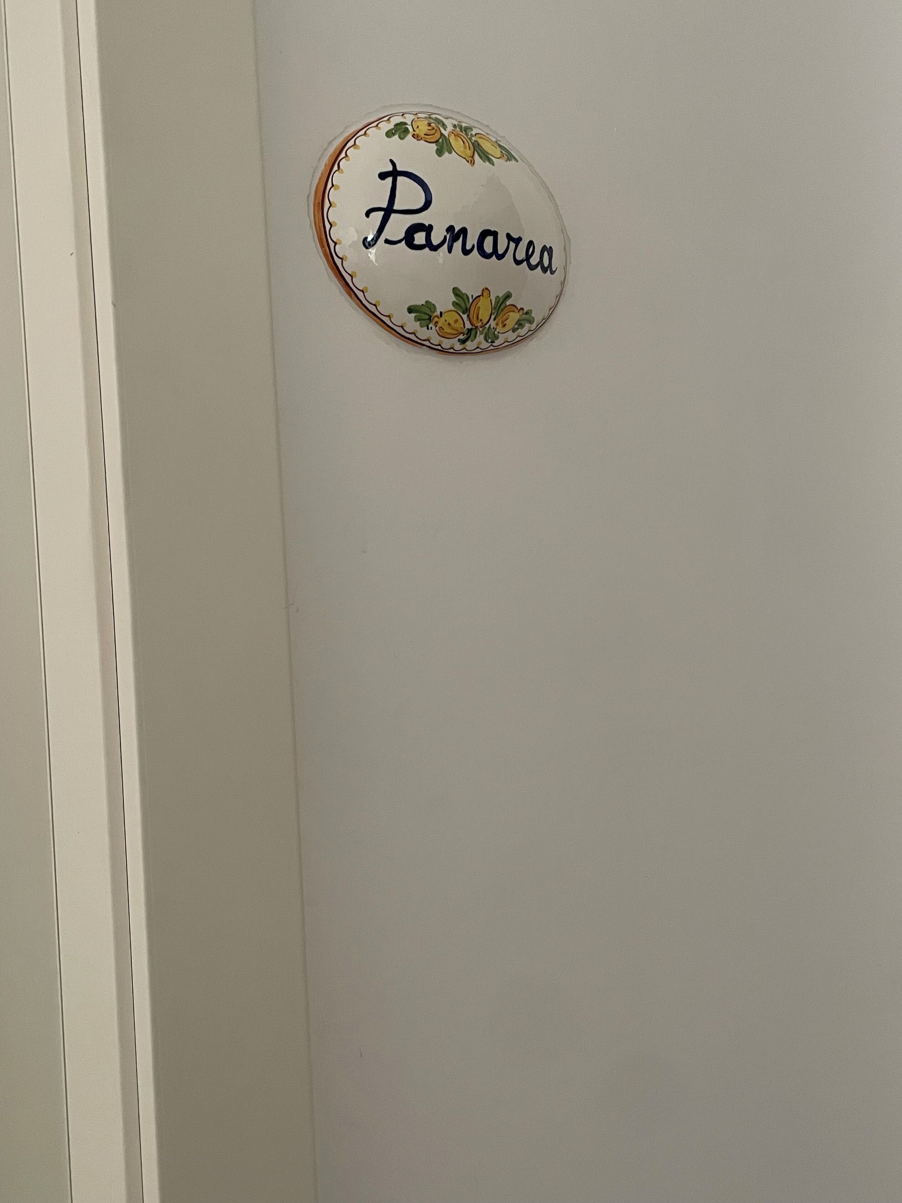 Een wandbord met de naam "Panarea", omgeven door een decoratieve rand met tekeningen van fruit.